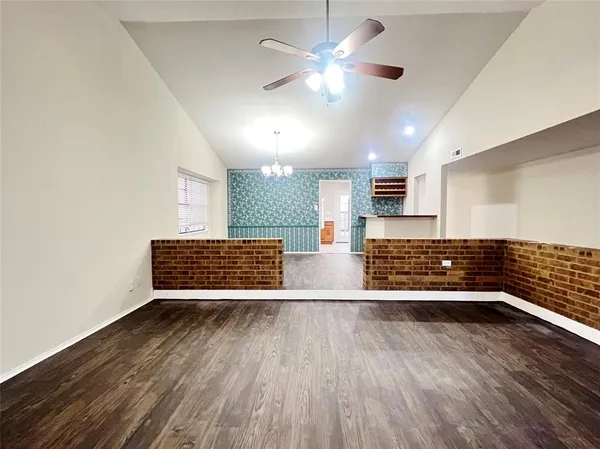 a view of an empty room with wooden floor and a kitchen