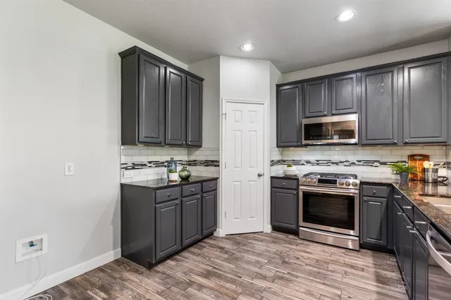 a kitchen with stainless steel appliances granite countertop a stove top oven a sink dishwasher a refrigerator and a microwave oven with wooden floor