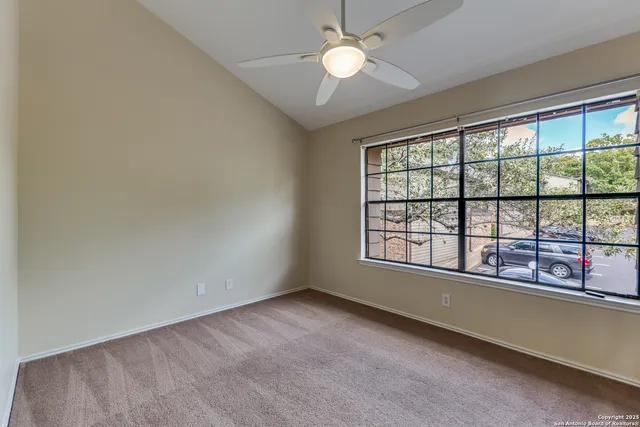 an empty room with chandelier fan and windows