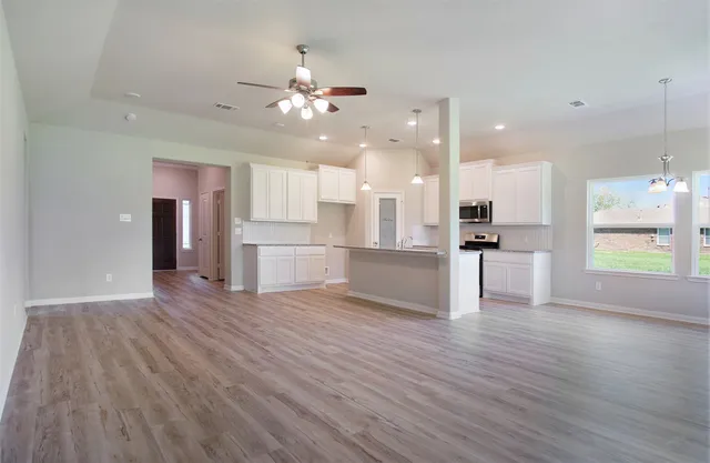 an empty room with wooden floor and kitchen view