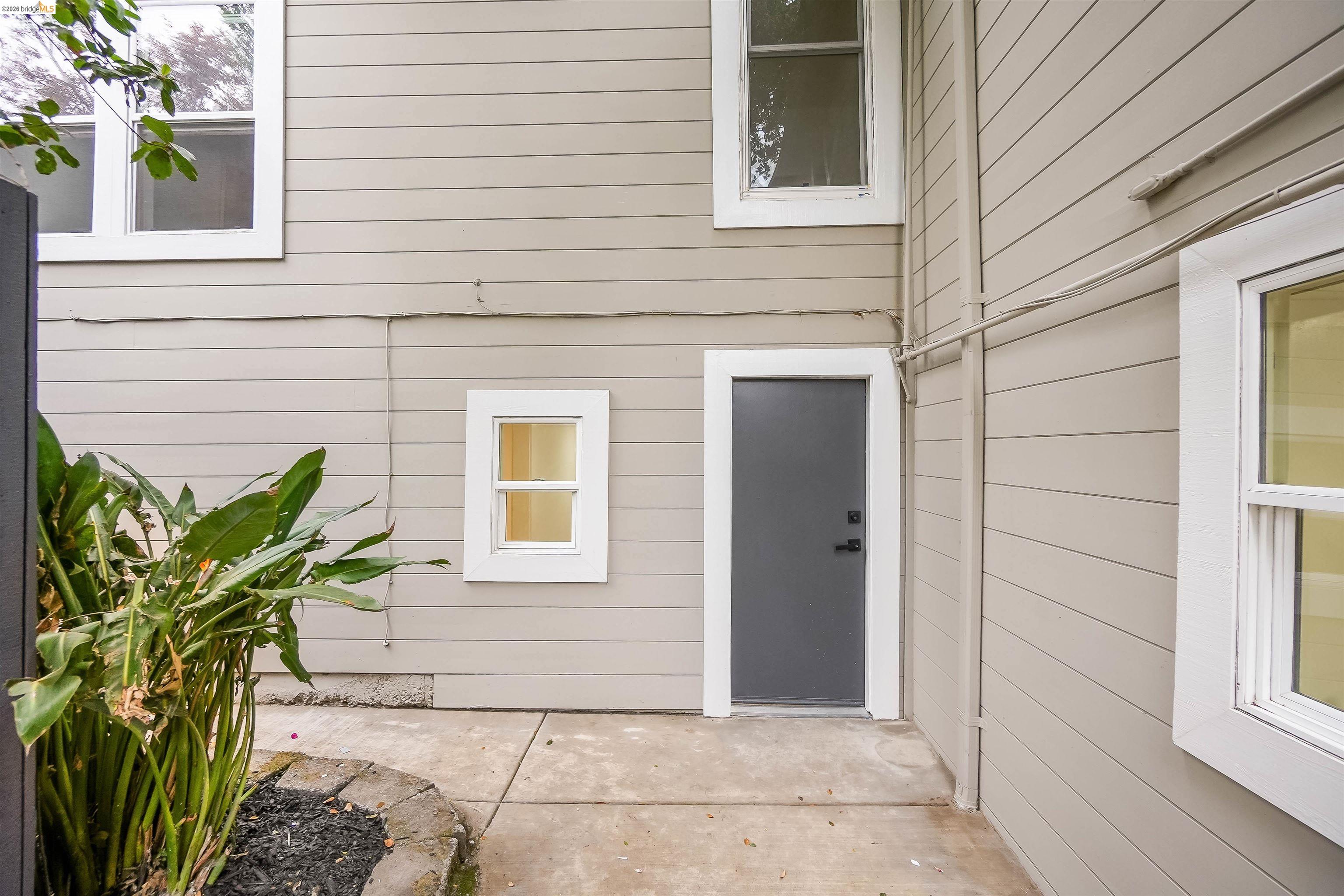 1812 Woolsey Street Berkeley, CA 94703 - Photo 32 of 48 Exterior siding in a light neutral tone featuring white window trim, a contemporary grey door, and concrete hardscaping