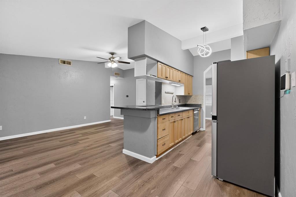 2309 Fyke Road Carrollton, TX 75006 - Photo 13 of 40 Open-concept living space featuring wood-finish flooring, a contemporary ceiling fan, and a kitchen with stainless steel appliances, light wood cabinetry, and a dark countertop