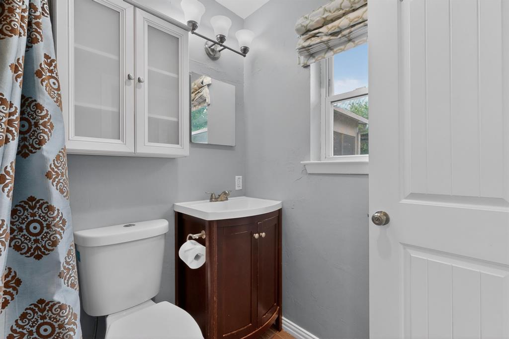 2309 Fyke Road Carrollton, TX 75006 - Photo 22 of 40 Bathroom featuring a dark wood-finish vanity with an integrated sink, wall-mounted light fixture, white upper cabinetry with frosted glass inserts, and a single pane window with a window treatment