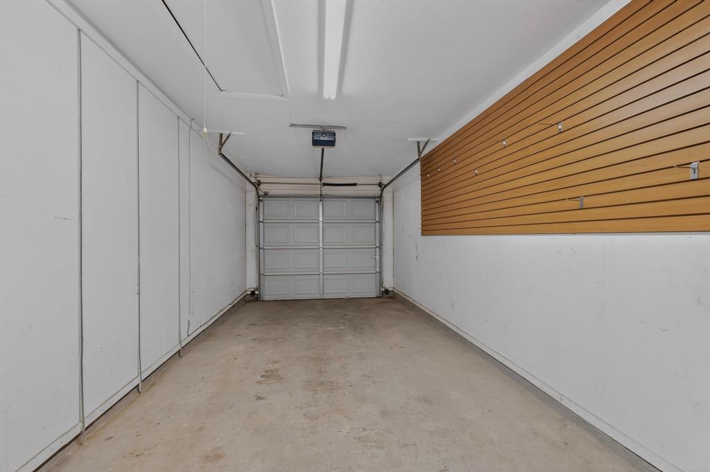 2309 Fyke Road Carrollton, TX 75006 - Photo 33 of 40 Attached garage featuring a concrete floor, automatic garage door opener, white painted walls, wood-finish slatwall storage system, and fluorescent lighting