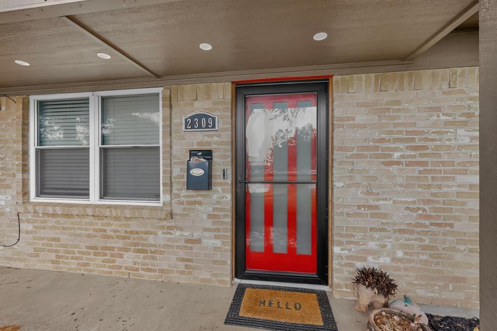 2309 Fyke Road Carrollton, TX 75006 - Photo 4 of 40 Brick exterior featuring a red entry door with black framing, white window frames, and a concrete porch