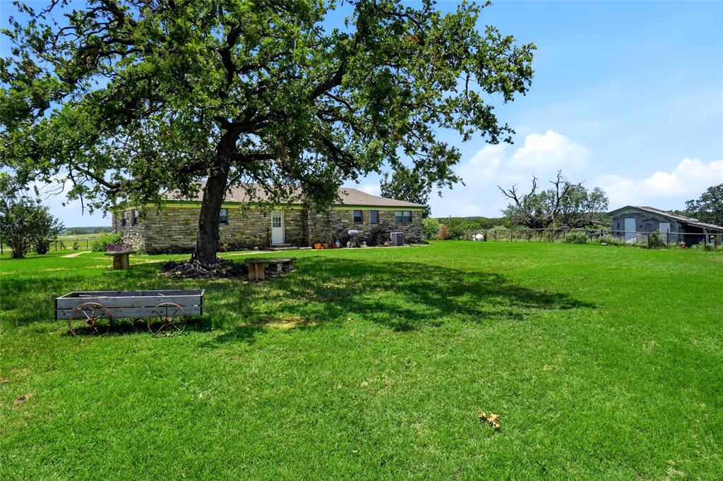 2186 Gilliland Road Springtown, TX 76082 - Photo 16 of 25 Expansive green lawn with a mature shade tree, stone exterior residence, and secondary outbuilding