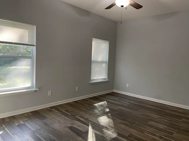 an empty room with wooden floor cabinet and windows