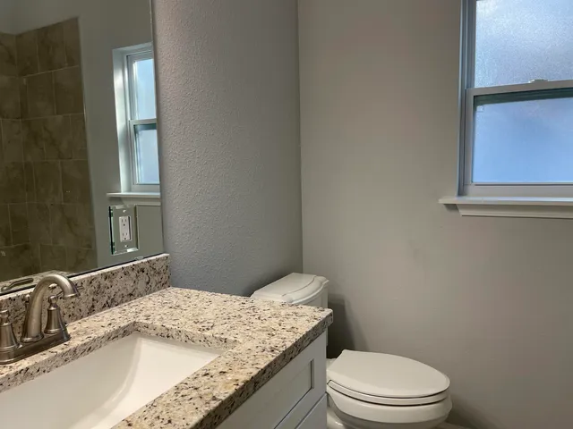 a bathroom with a granite countertop toilet sink and mirror