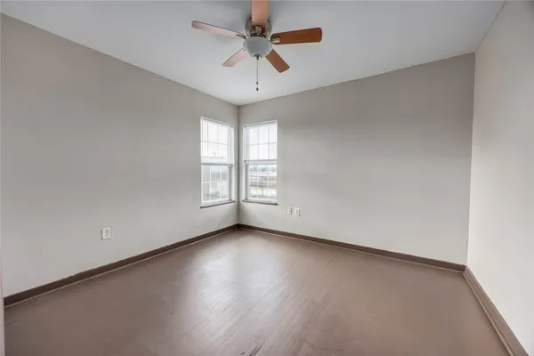 an empty room with wooden floor chandelier fan and windows