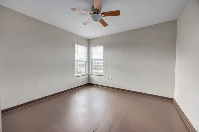 an empty room with wooden floor chandelier fan and windows