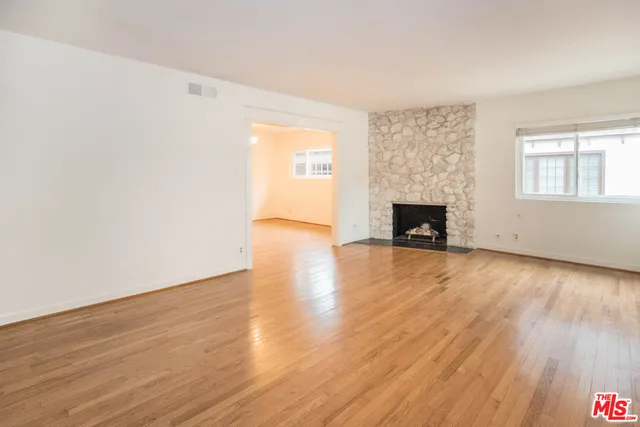 an empty room with wooden floor fireplace and windows