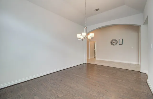 an empty room with a chandelier fan and wooden floor