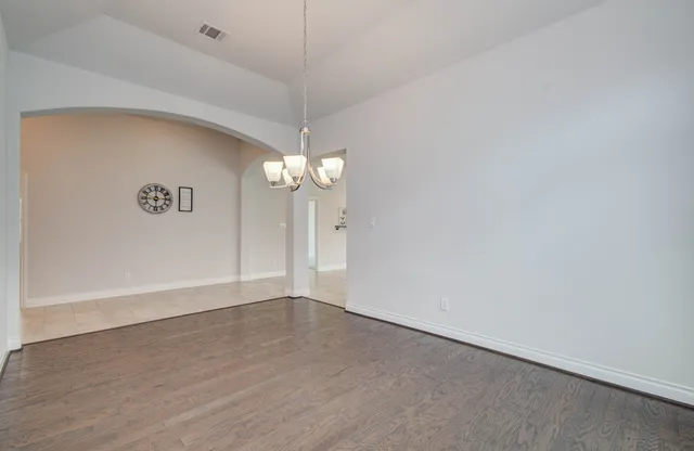 an empty room with a chandelier fan and wooden floor