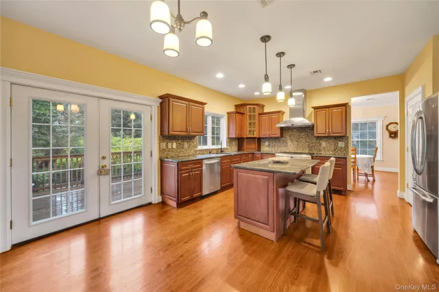 a kitchen with stainless steel appliances kitchen island granite countertop a stove a refrigerator a oven a sink a dining table and chairs with wooden floor