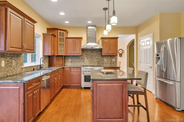 a kitchen with stainless steel appliances granite countertop a refrigerator a sink dishwasher a stove and a dining table with wooden floor