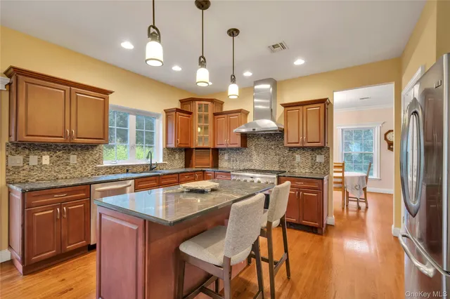 a kitchen with stainless steel appliances granite countertop wooden cabinets a refrigerator a sink a stove and a wooden cabinets