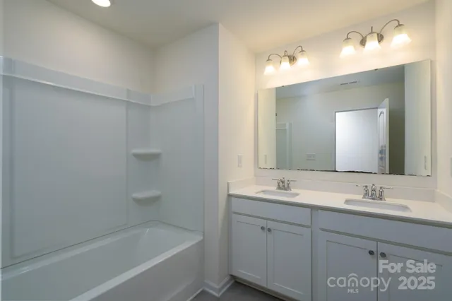 a bathroom with a tub sink double vanity and a mirror