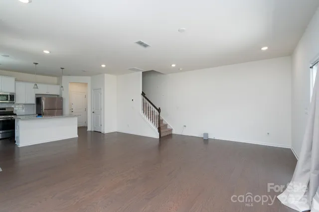 an empty room with wooden floor and a kitchen