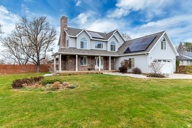 View of front of property with covered porch, roof with shingles, solar panels, a chimney, and an attached garage