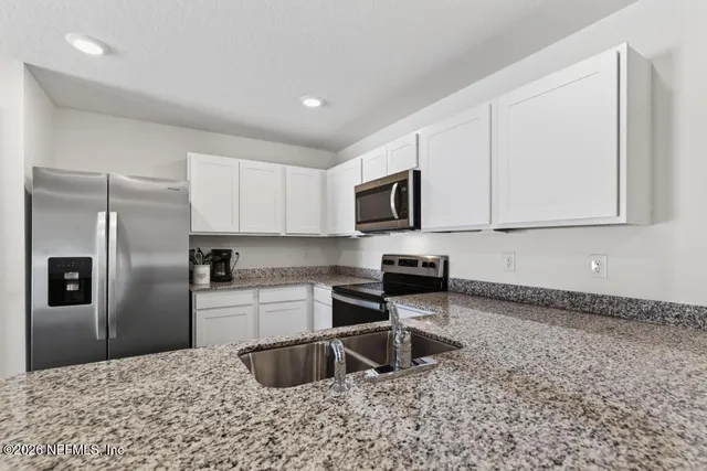 a kitchen with stainless steel appliances granite countertop a refrigerator a stove a sink and white cabinets