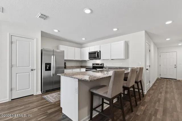 a kitchen with stainless steel appliances granite countertop a dining table chairs refrigerator and microwave