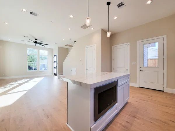 a view of an empty room with wooden floor and a kitchen