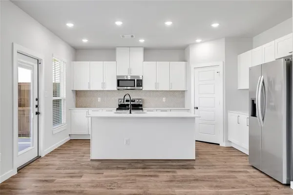 a kitchen with stainless steel appliances a refrigerator stove a sink and white cabinets with wooden floor