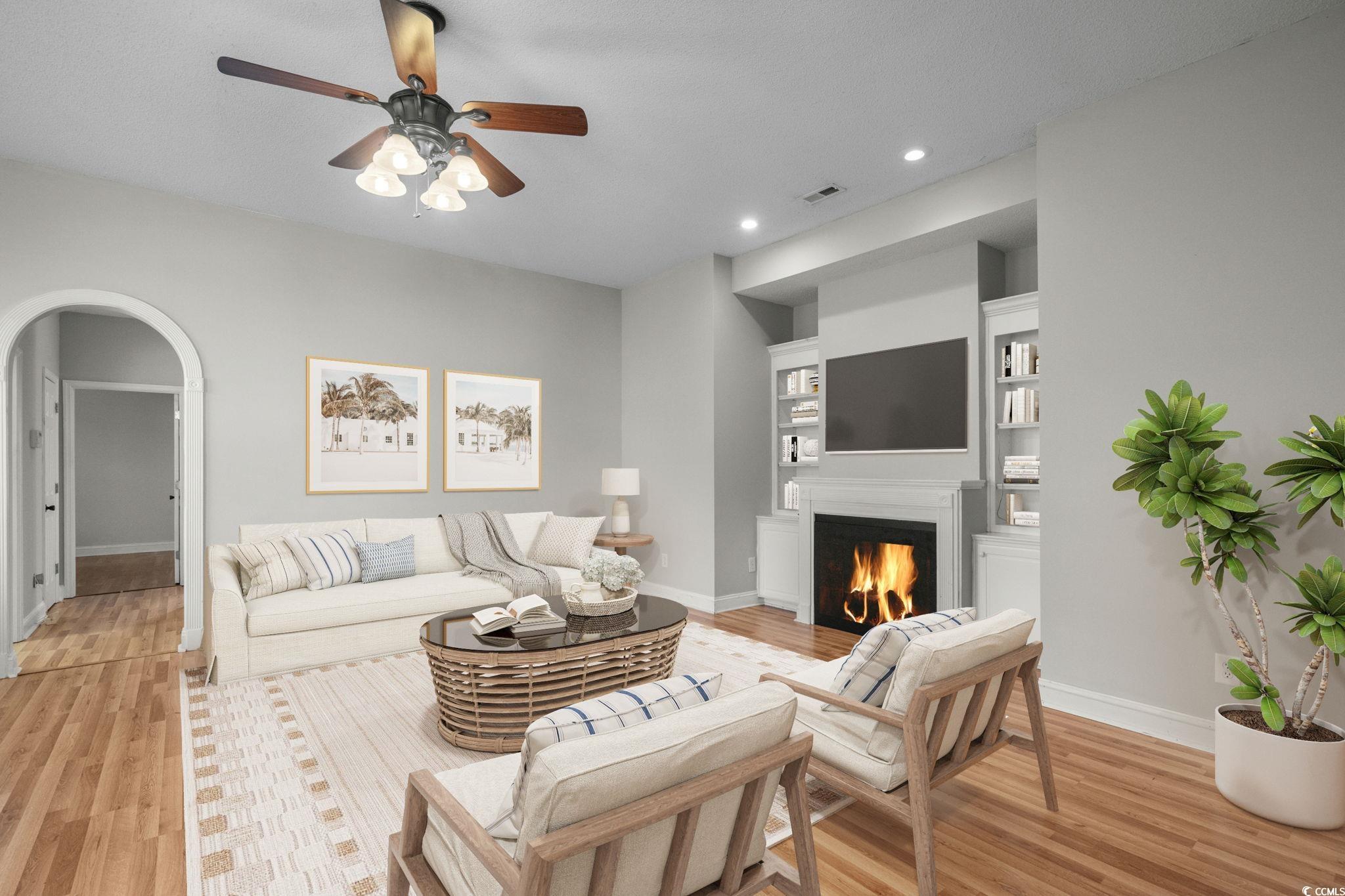 2723 Canvasback Trail Myrtle Beach, SC 29588 - Photo 6 of 40 Living room with arched walkways, built in shelves, a warm lit fireplace, light wood-style flooring, and recessed lighting
