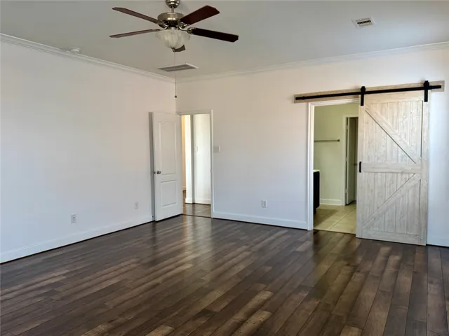 a view of an empty room with wooden floor and a ceiling fan