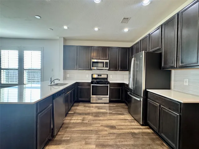 a large kitchen with a large counter top a sink stainless steel appliances and cabinets