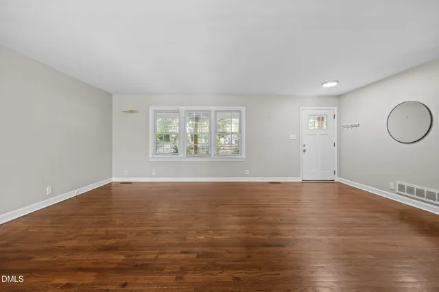 a view of an empty room with wooden floor and window