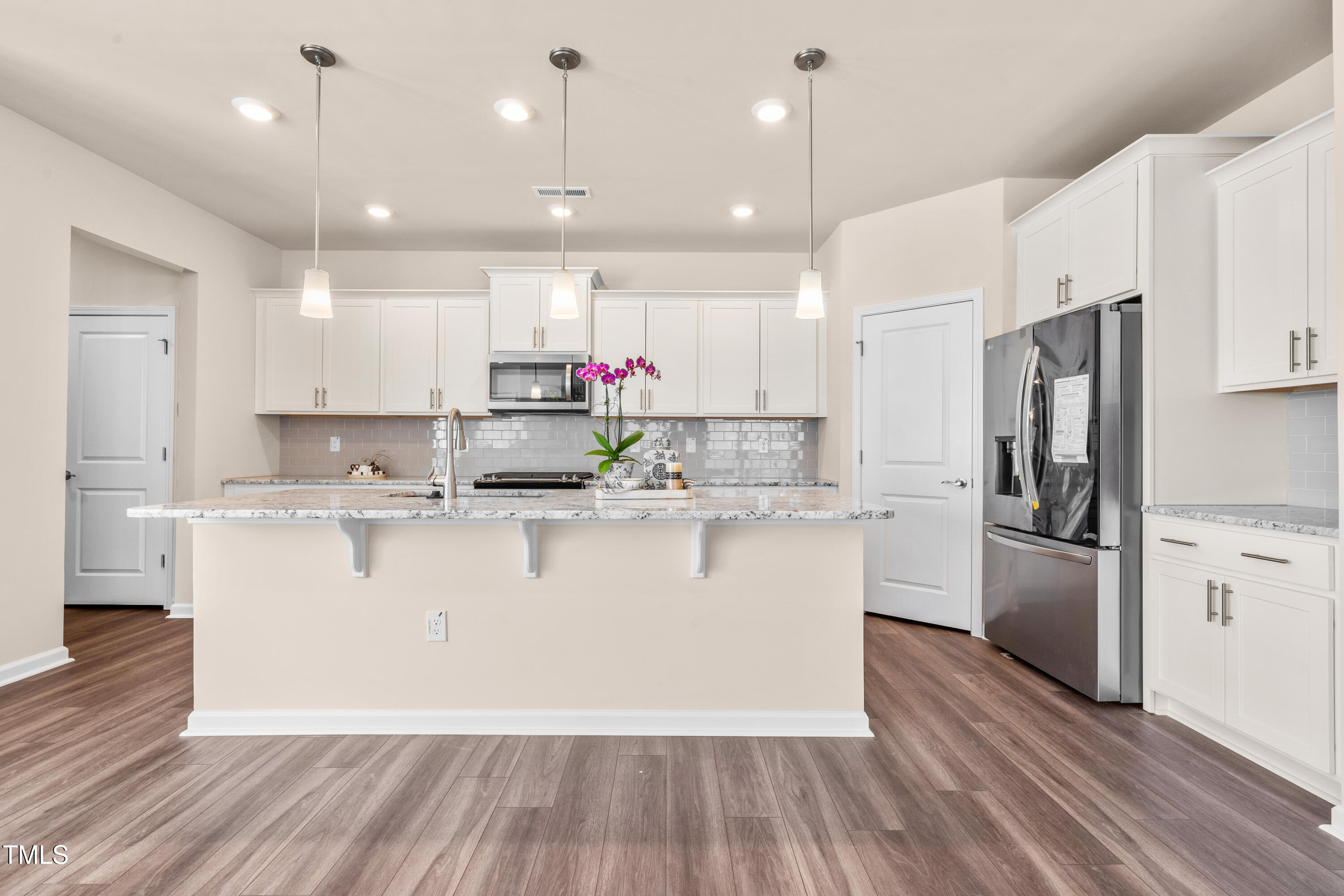 5800 Agrinio Way Raleigh, NC 27603 - Photo 5 of 38 a large white kitchen with kitchen island a refrigerator a stove a sink dishwasher a oven and a dining table with wooden floor