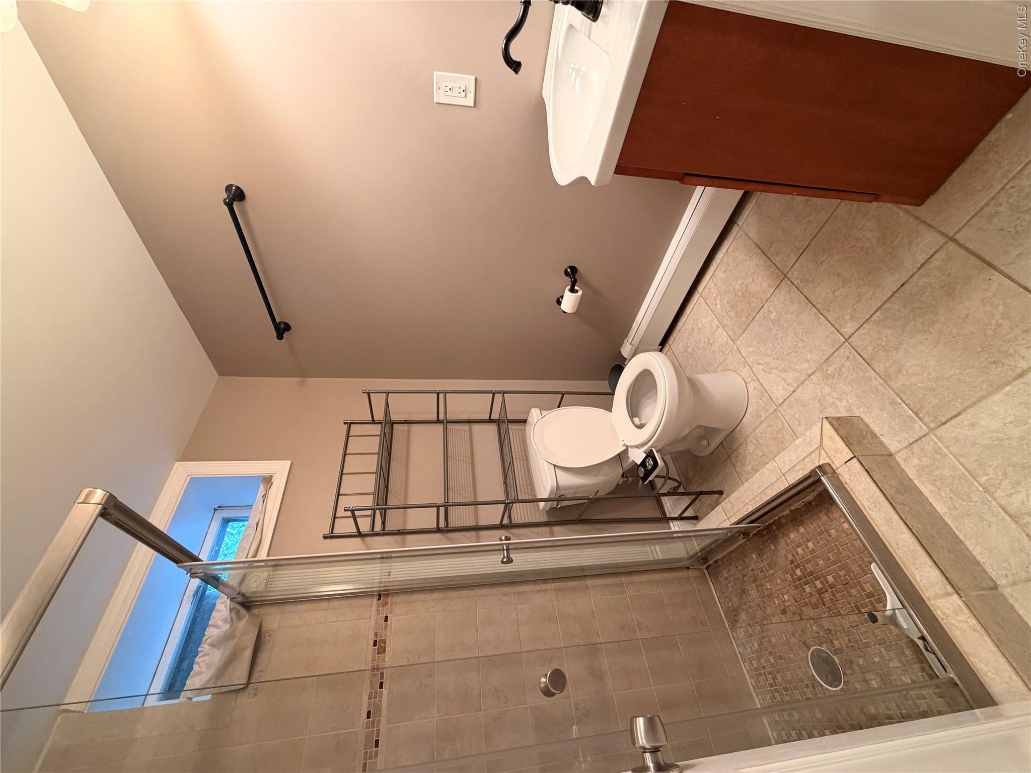 157 Brewer Road, Unit 1A Newburgh, NY 12550 - Photo 4 of 8 Bathroom featuring a glass-enclosed shower with tile surround and mosaic floor, a single vanity with a white basin and dark-toned cabinet, and neutral tile flooring