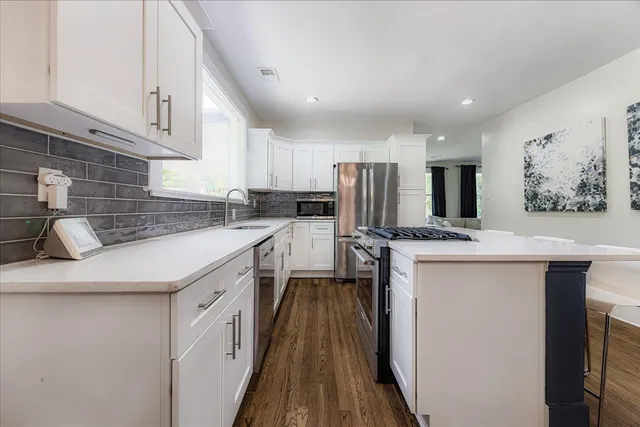 a kitchen with a sink a stove top oven a refrigerator with white cabinets and wooden floor