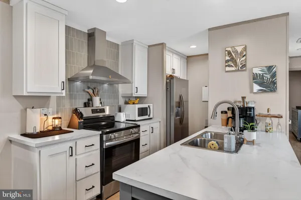 a kitchen with stainless steel appliances kitchen island granite countertop a refrigerator a stove a sink dishwasher and white cabinets with wooden floor