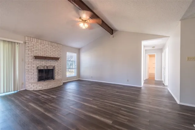 a view of an empty room with wooden floor fireplace and a window
