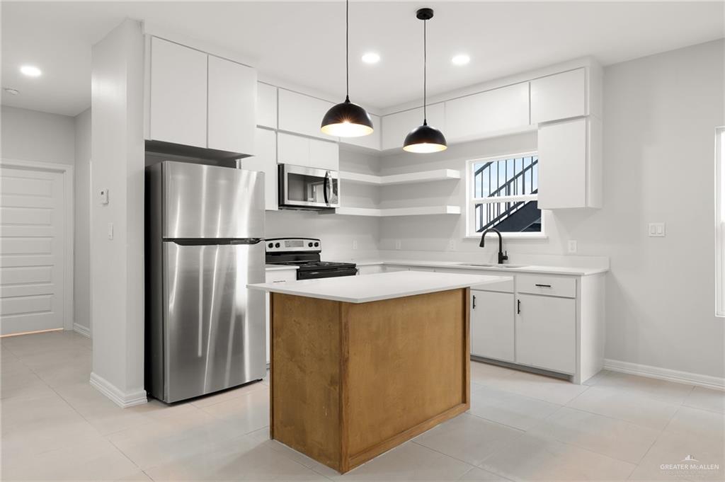 4217 Hummingbird Avenue McAllen, TX 78504 - Photo 12 of 15 Kitchen featuring open shelves, appliances with stainless steel finishes, white cabinets, a center island, and decorative light fixtures