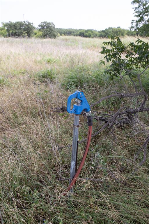 497 Big Sandy Road Newcastle, TX 76372 - Photo 5 of 22 Outdoor water spigot with a blue handle, situated in a field of natural grasses, surrounded by mature trees in the distance