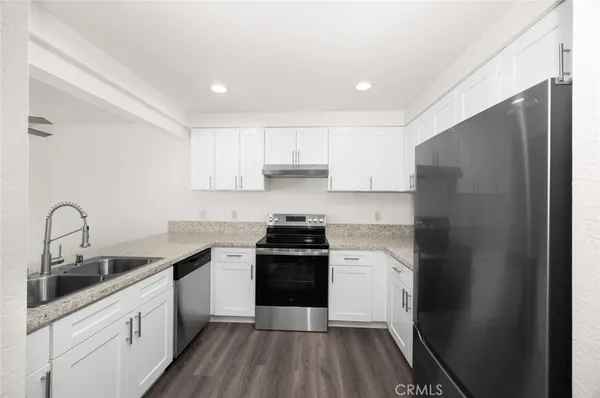 a kitchen with a sink dishwasher a refrigerator and white cabinets with wooden floor