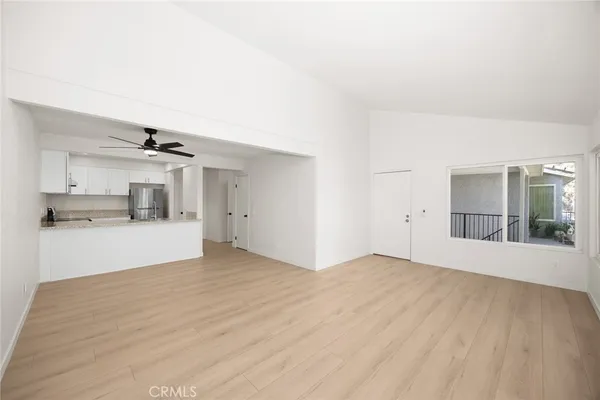 a view of empty room with wooden floor and kitchen view