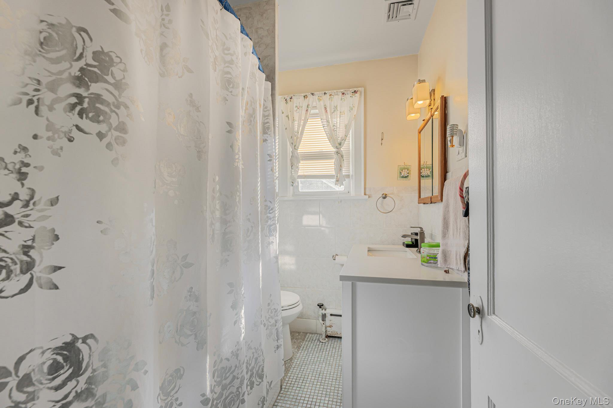168 Stephenson Boulevard New Rochelle, NY 10801 - Photo 13 of 21 Full bath with vanity, tile walls, a shower with shower curtain, a wainscoted wall, and light tile patterned flooring