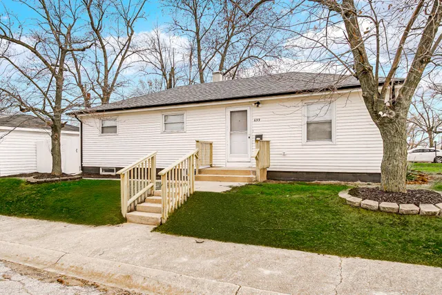 a view of a white house next to a yard with big trees
