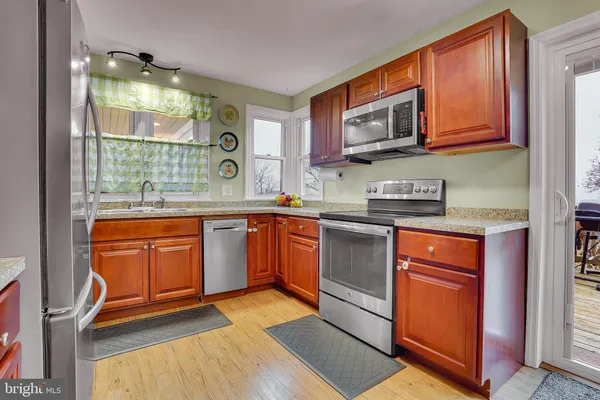 a kitchen with stainless steel appliances granite countertop wooden cabinets a stove a sink and a large window