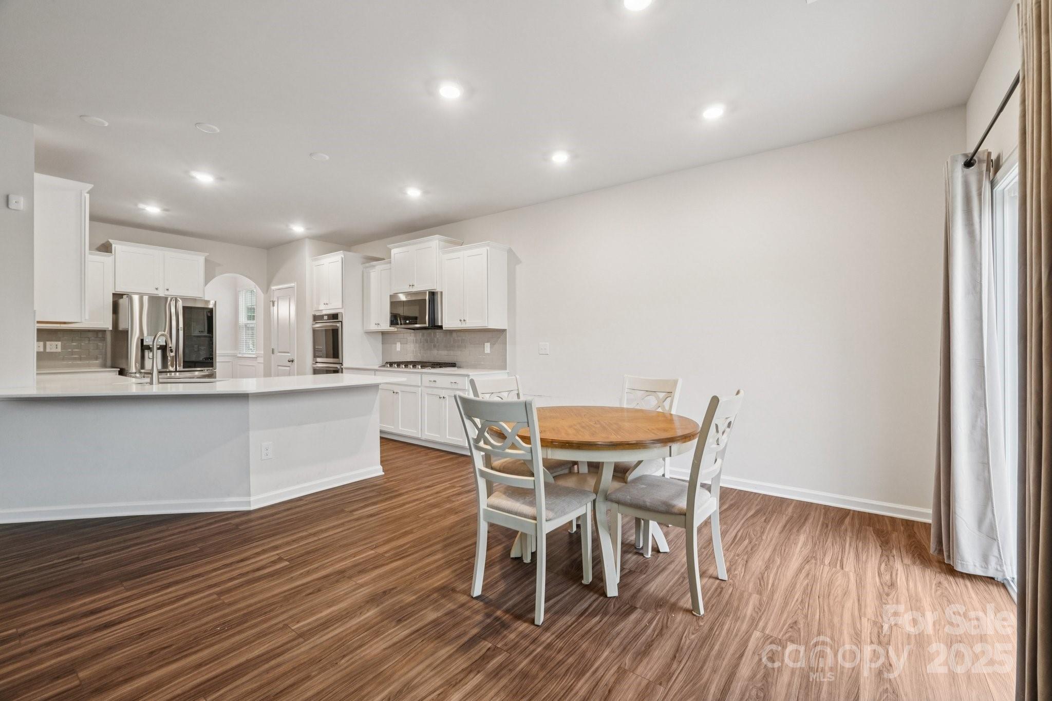 299 Hamptons Cove Road Troutman, NC 28166 - Photo 12 of 40 a kitchen with stainless steel appliances kitchen island granite countertop a wooden table and chairs