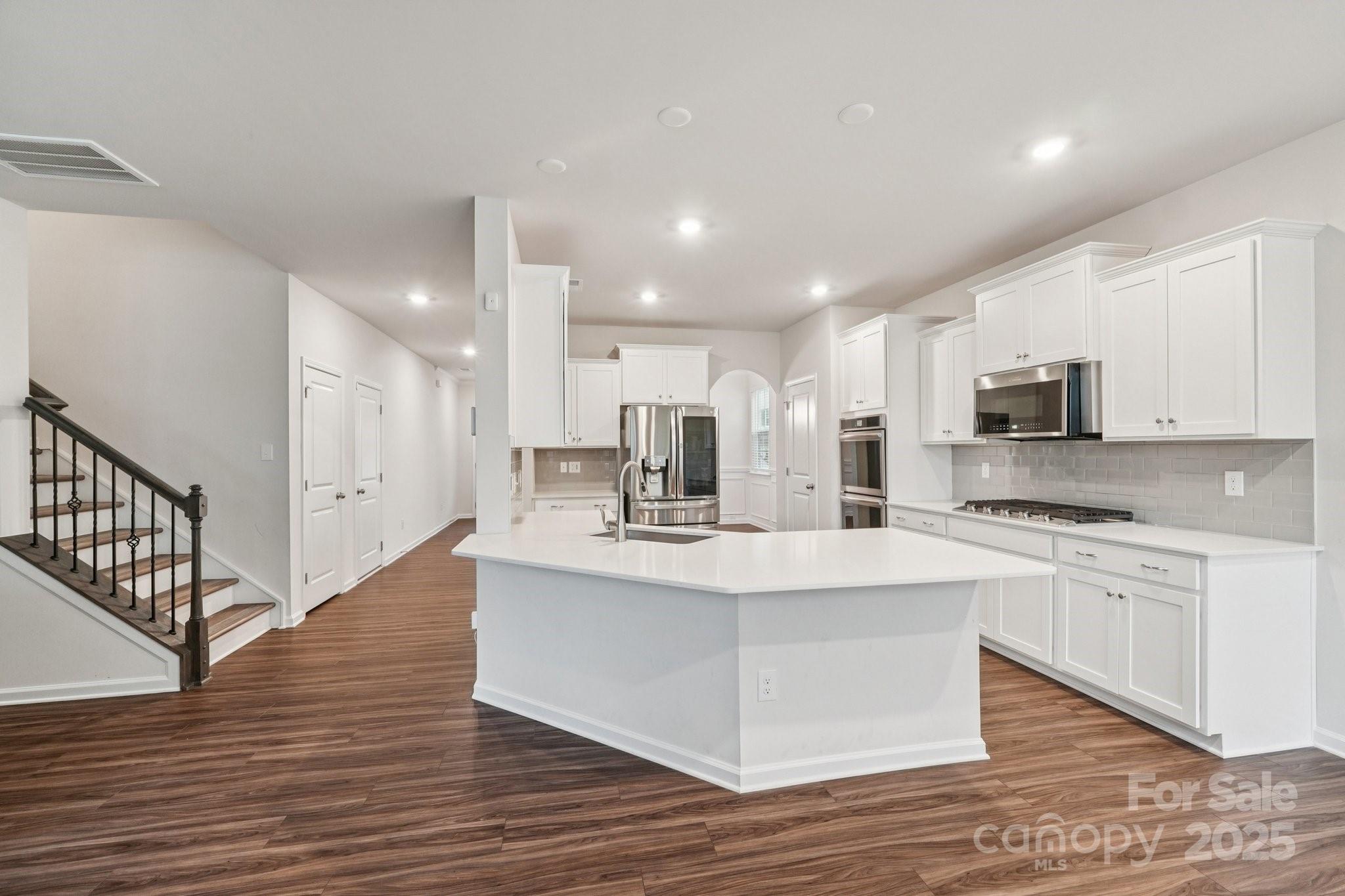 299 Hamptons Cove Road Troutman, NC 28166 - Photo 10 of 40 a large white kitchen with kitchen island a sink wooden floor and stainless steel appliances