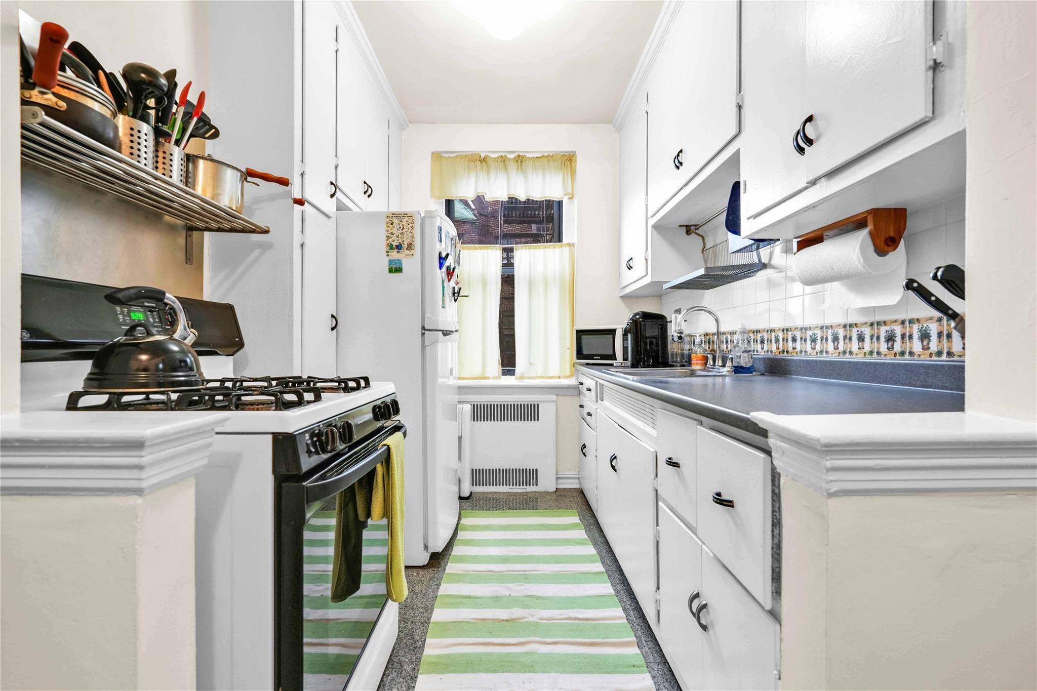 84-51 Beverly Road, Unit 5P Queens, NY 11415 - Photo 9 of 19 Kitchen featuring radiator heating unit, black gas range, white cabinets, and backsplash