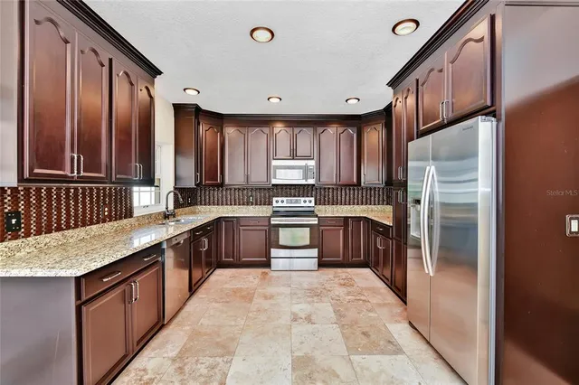 a large kitchen with stainless steel appliances granite countertop a stove refrigerator and a sink