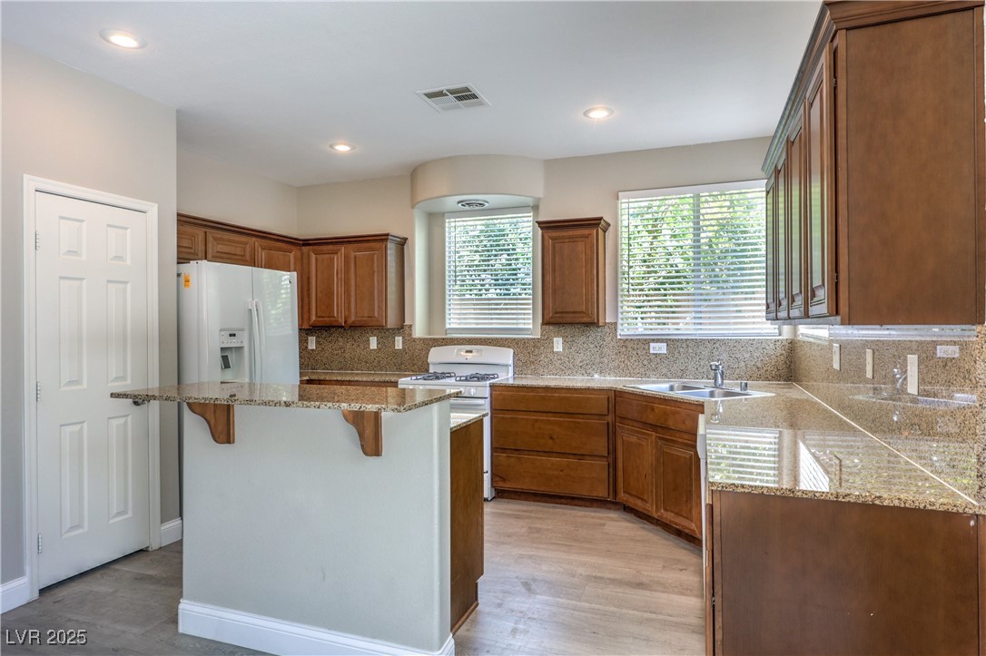 585 Foster Springs Road Las Vegas, NV 89148 - Photo 15 of 39 Kitchen with white appliances, a breakfast bar, light wood-style floors, tasteful backsplash, and brown cabinets