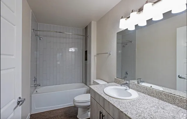 a bathroom with a granite countertop sink toilet mirror and bathtub