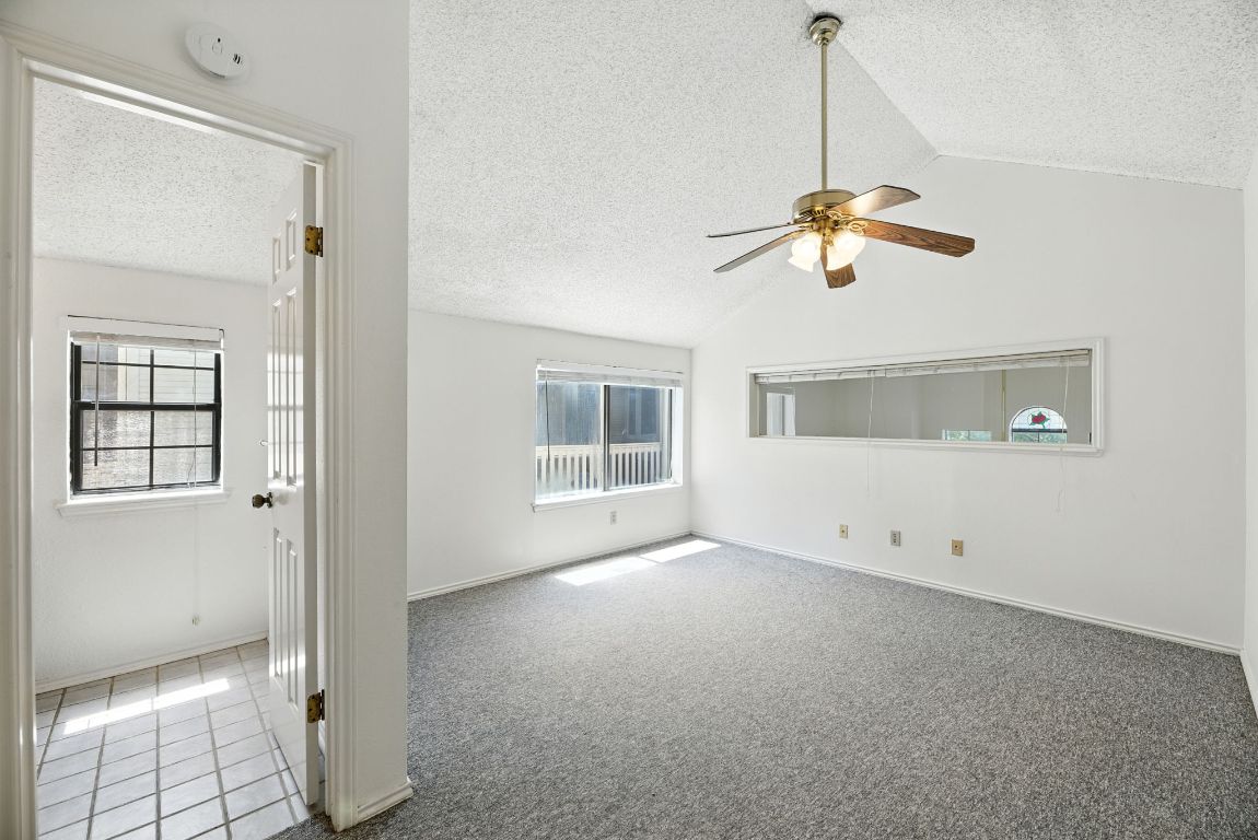 4409 Speedway, Unit 201 Austin, TX 78751 - Photo 12 of 16 Carpeted empty room with a textured ceiling, vaulted ceiling, plenty of natural light, a ceiling fan, and tile patterned flooring